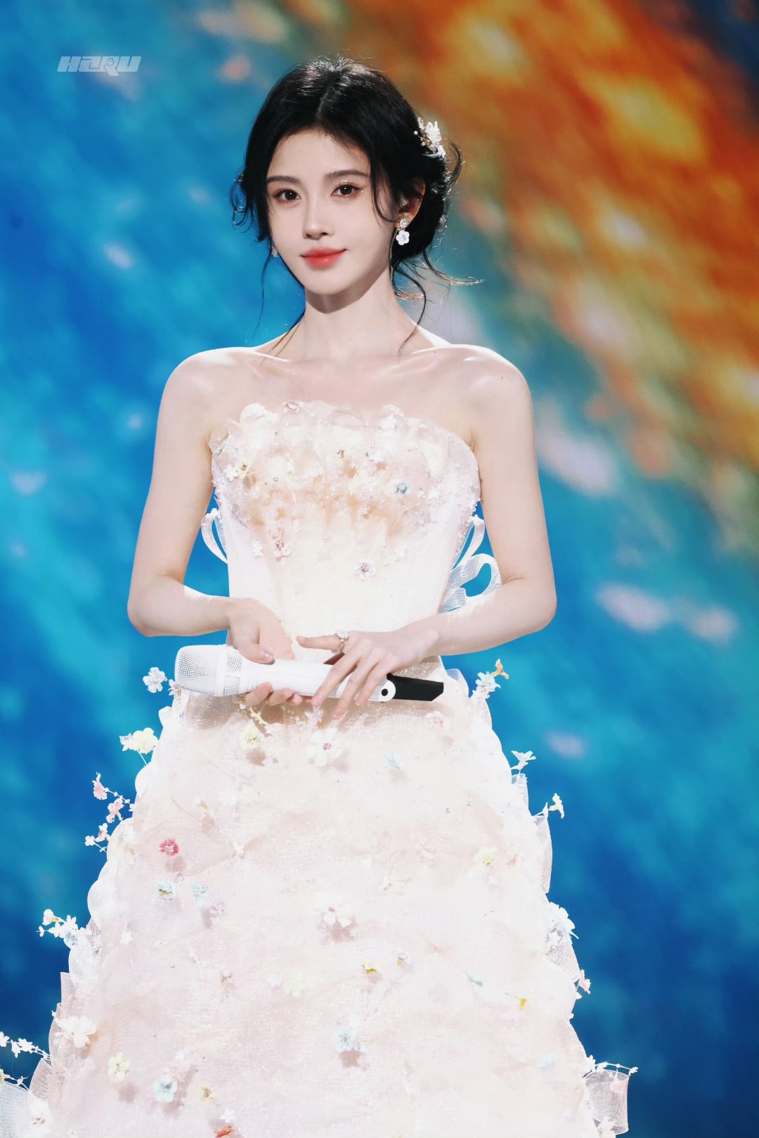 鞠婧祎美如仙子,一袭白裙优雅动人,手持话筒,光彩照人