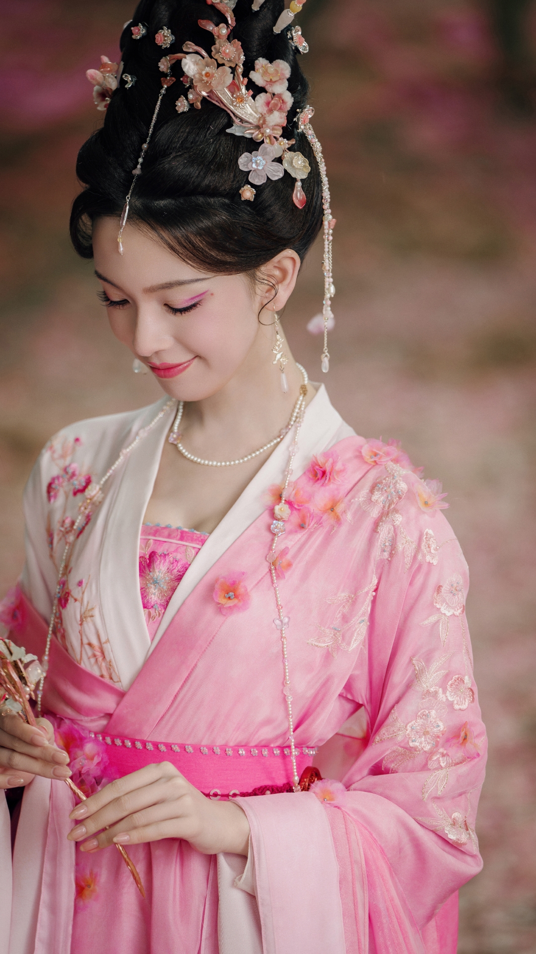 一身粉色繁花古装搭配精致花钿,发髻上满是花朵发饰,在花海背景里宛如