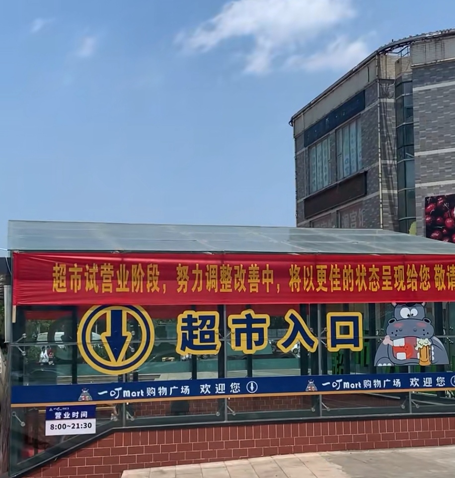 见下图:红色横幅上醒目印刷着: 超市试营业阶段,努力调整改善中,揭栽