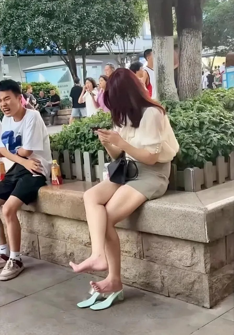 景区一角,美女光着脚丫在休闲的刷手机,坐在旁边的哥们这一脸的表情