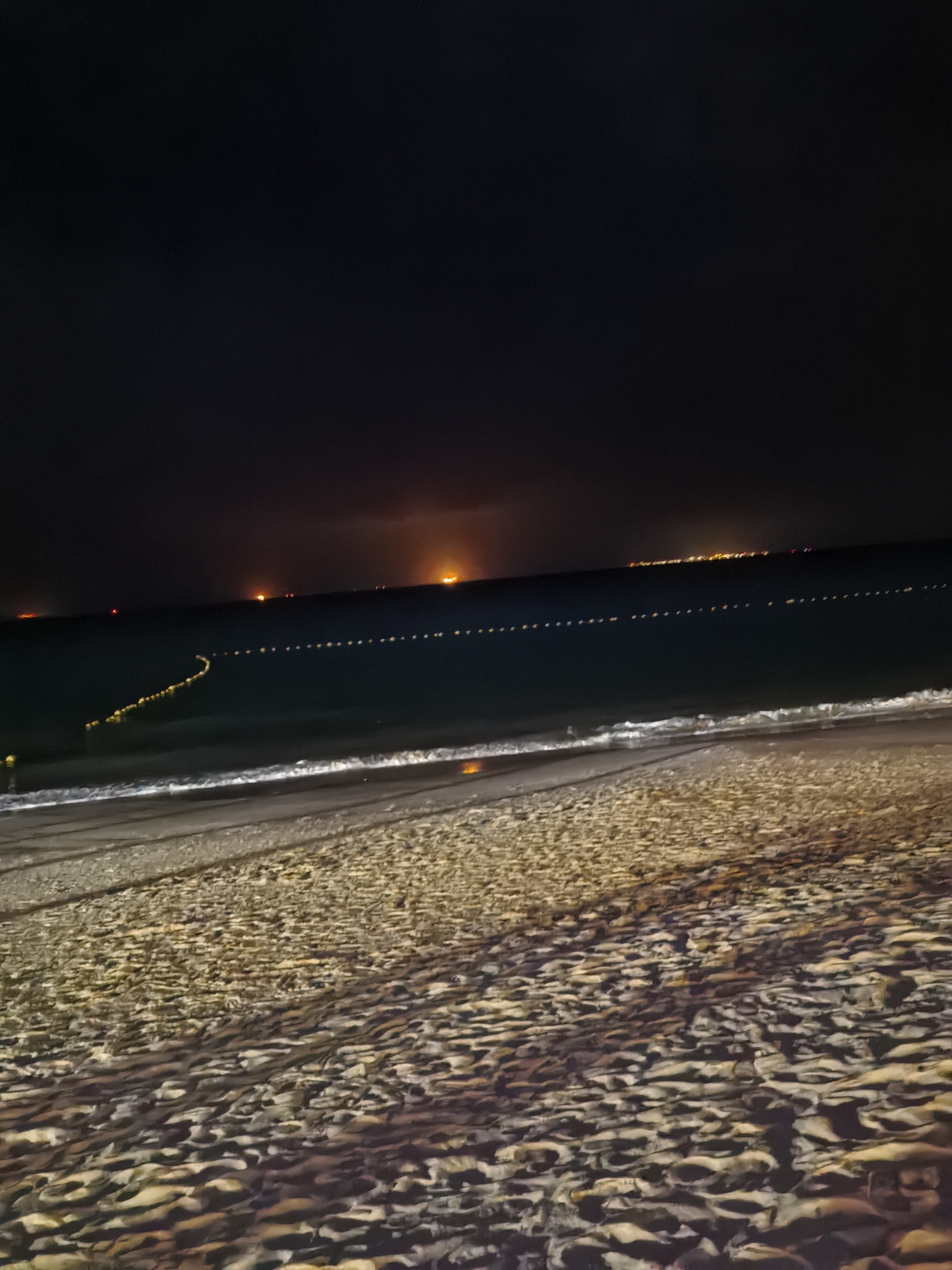 夜晚的海边,沙滩上留下一串脚印,远处城市灯光闪烁.#治愈系风景