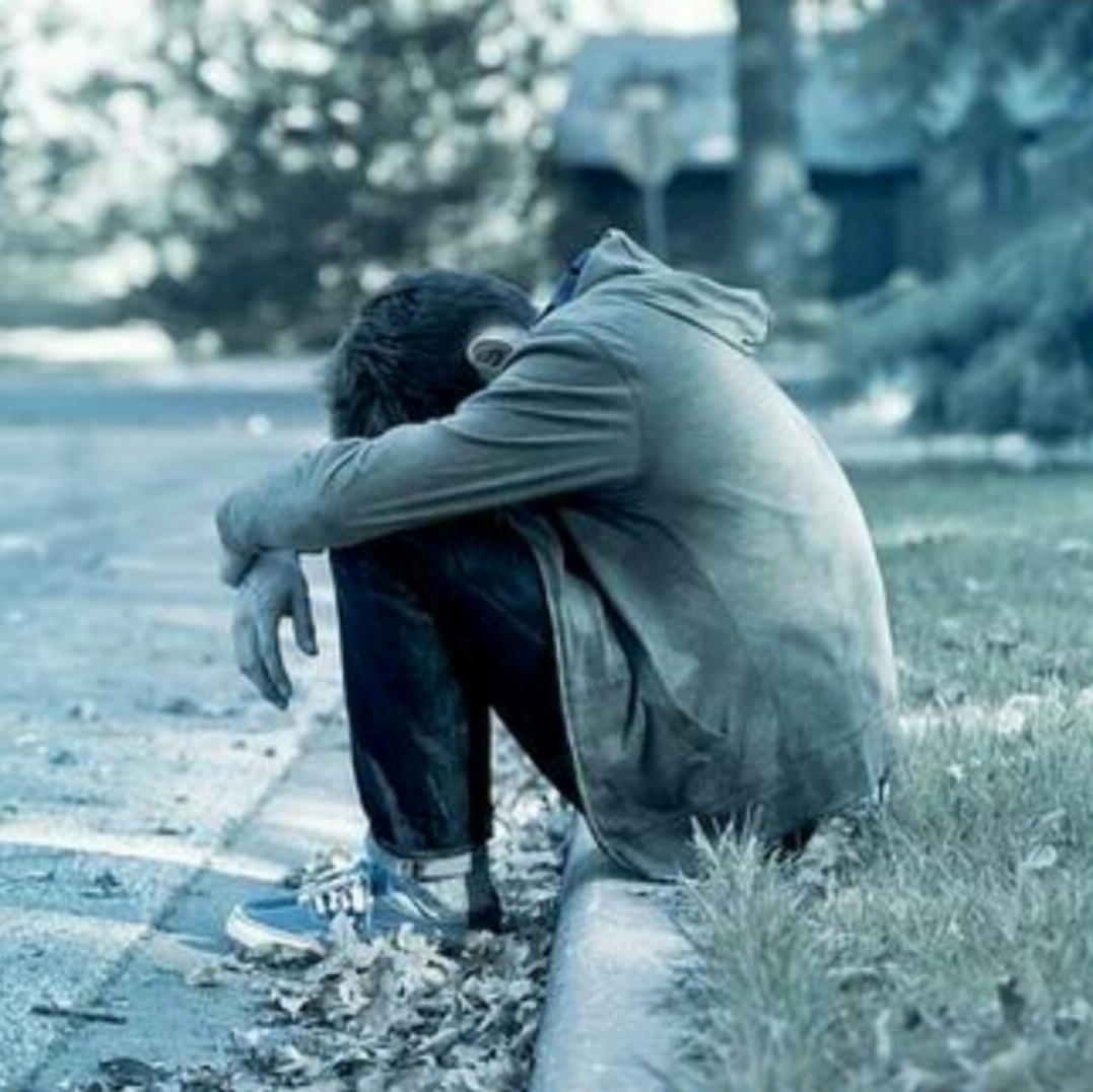 他坐在路边,身穿一件棕色外套,双手放在膝盖上