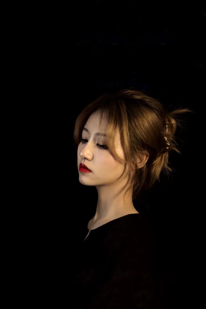 在这张光影交错的照片中,一位女子身着黑色上衣,站在深色调的背景下