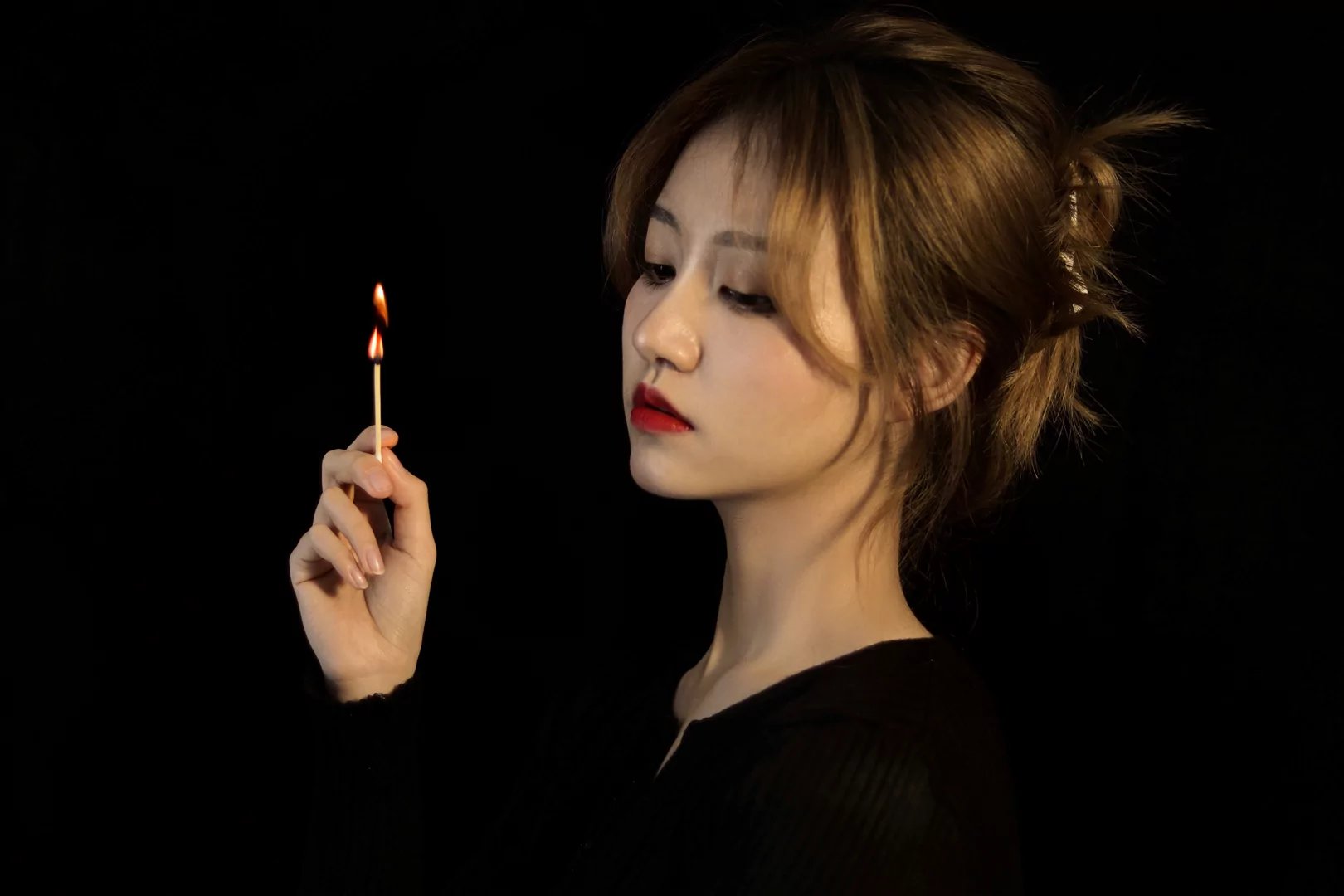 在这张光影交错的照片中,一位女子身着黑色上衣,站在深色调的背景下